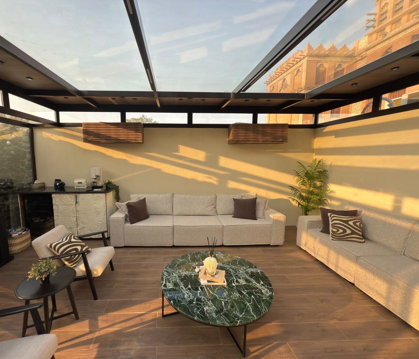 Glass room lounge at golden hour with linen sofas and a round green marble table